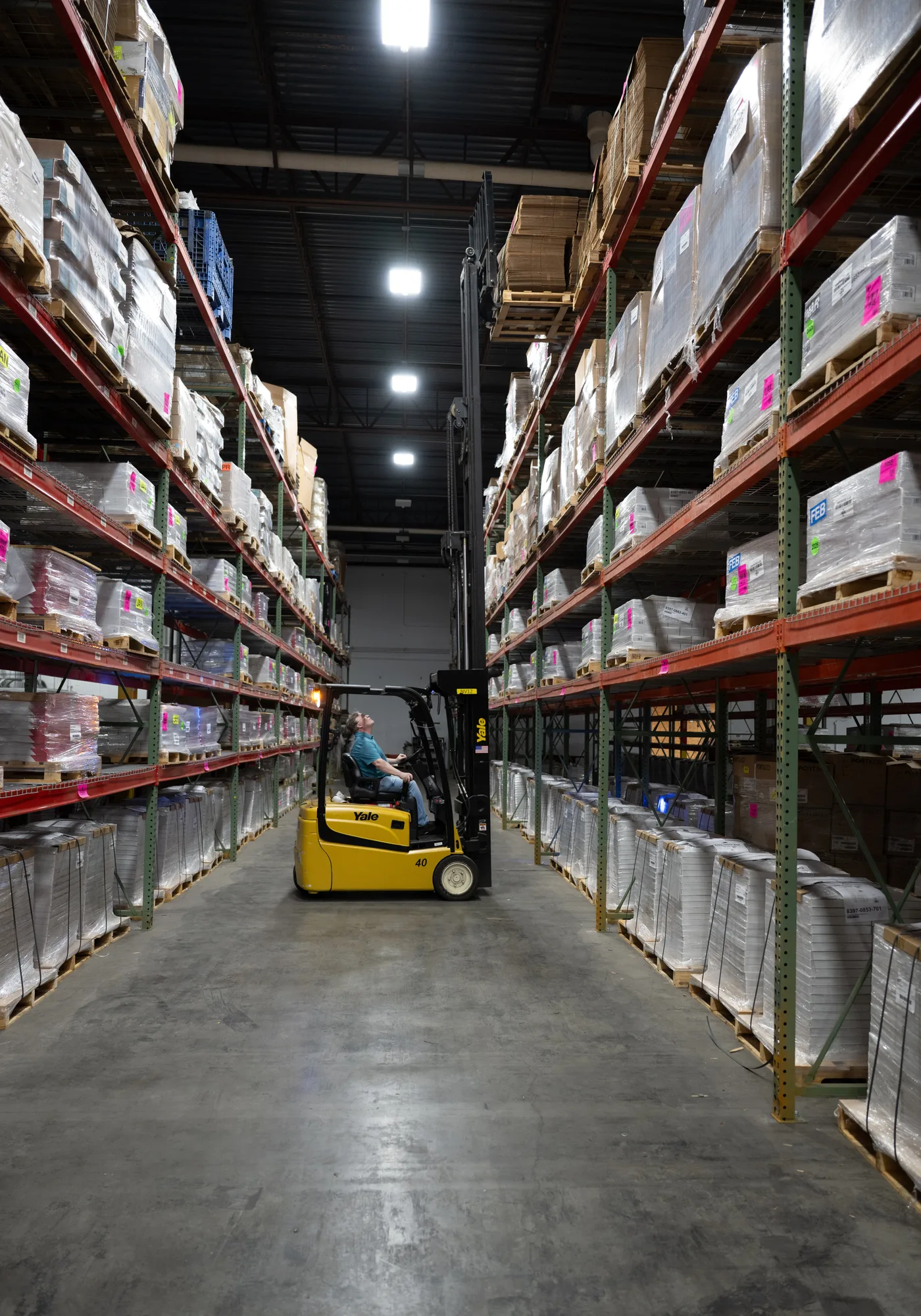 Forklift with mast extended placing a pallet on the top rack level